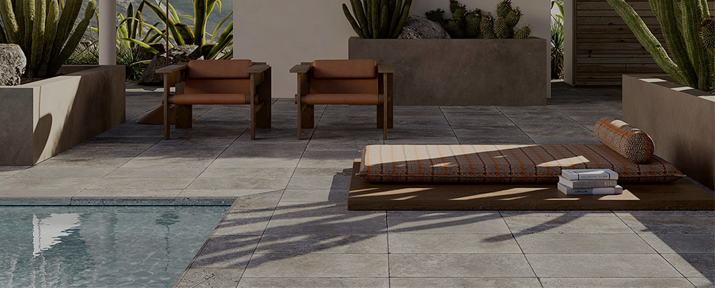 Outdoor terrace paved in grey stone-look porcelain beside a pool, with timber lounge chairs and cacti